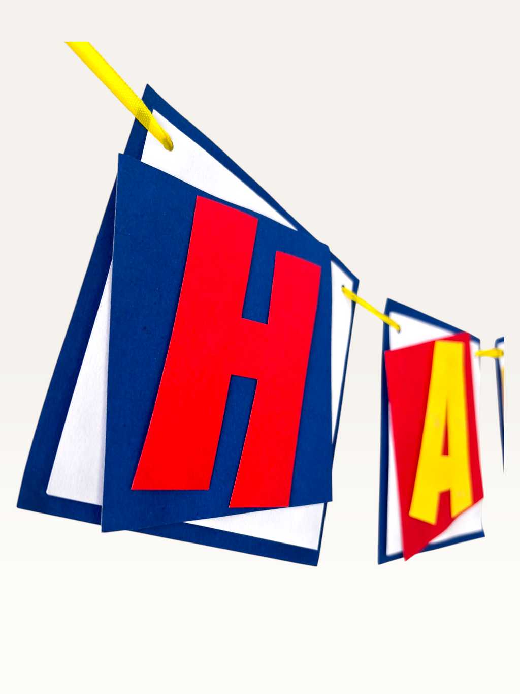 Paper Party Studio superhero birthday banner with layered red, yellow, and blue paper flags on a yellow string
