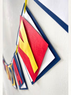 Paper Party Studio superhero birthday banner featuring layered red, yellow, and blue paper flags with dimensional text