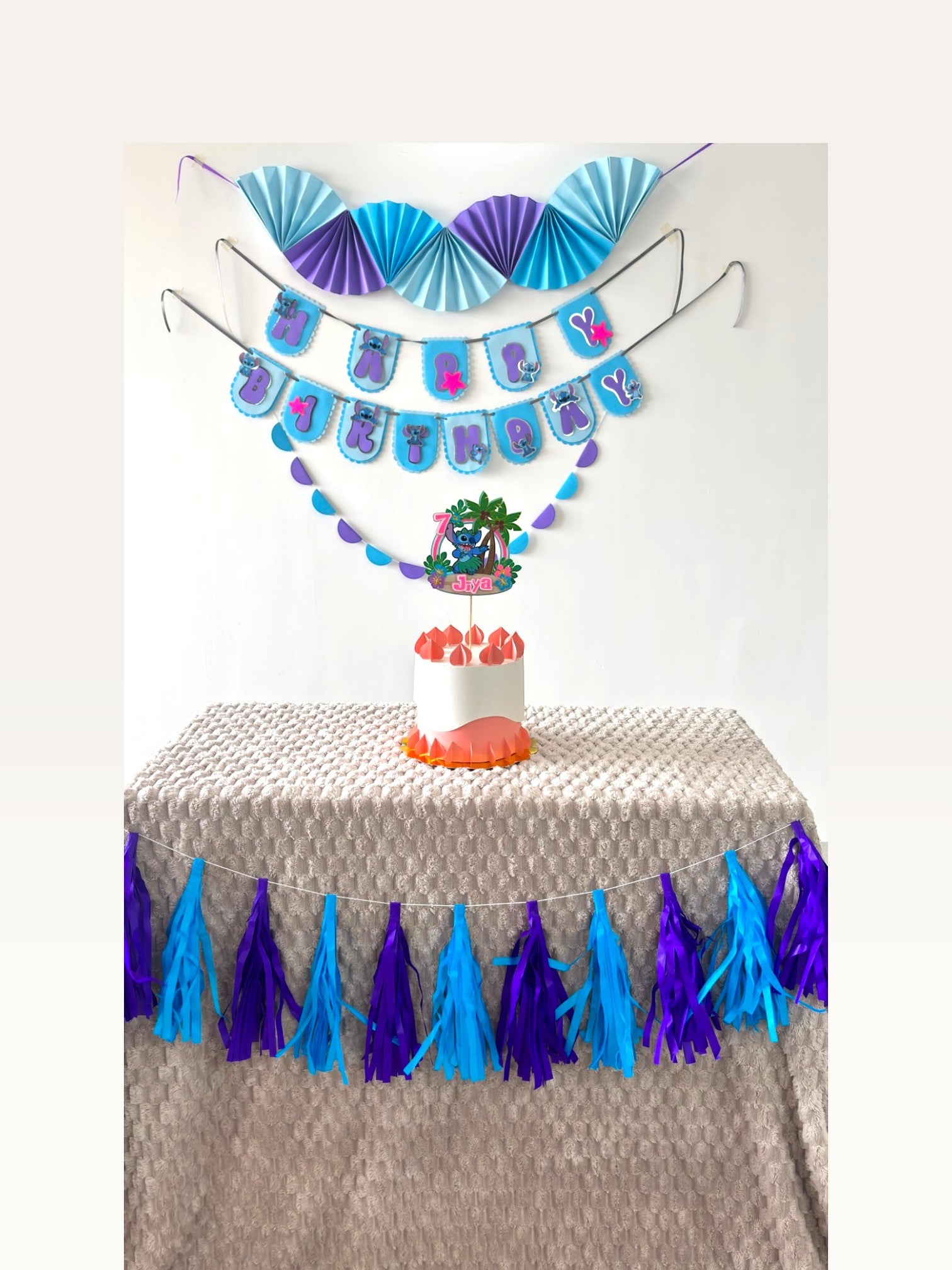 Paper Party Studio tropical luau birthday set with blue alien cake topper, paper fans, banner, and tassel garland.