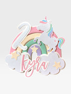 Paper Party Studio pastel rainbow unicorn cake topper with clouds, stars, custom name and age. Made of cardstock with glitter accents.