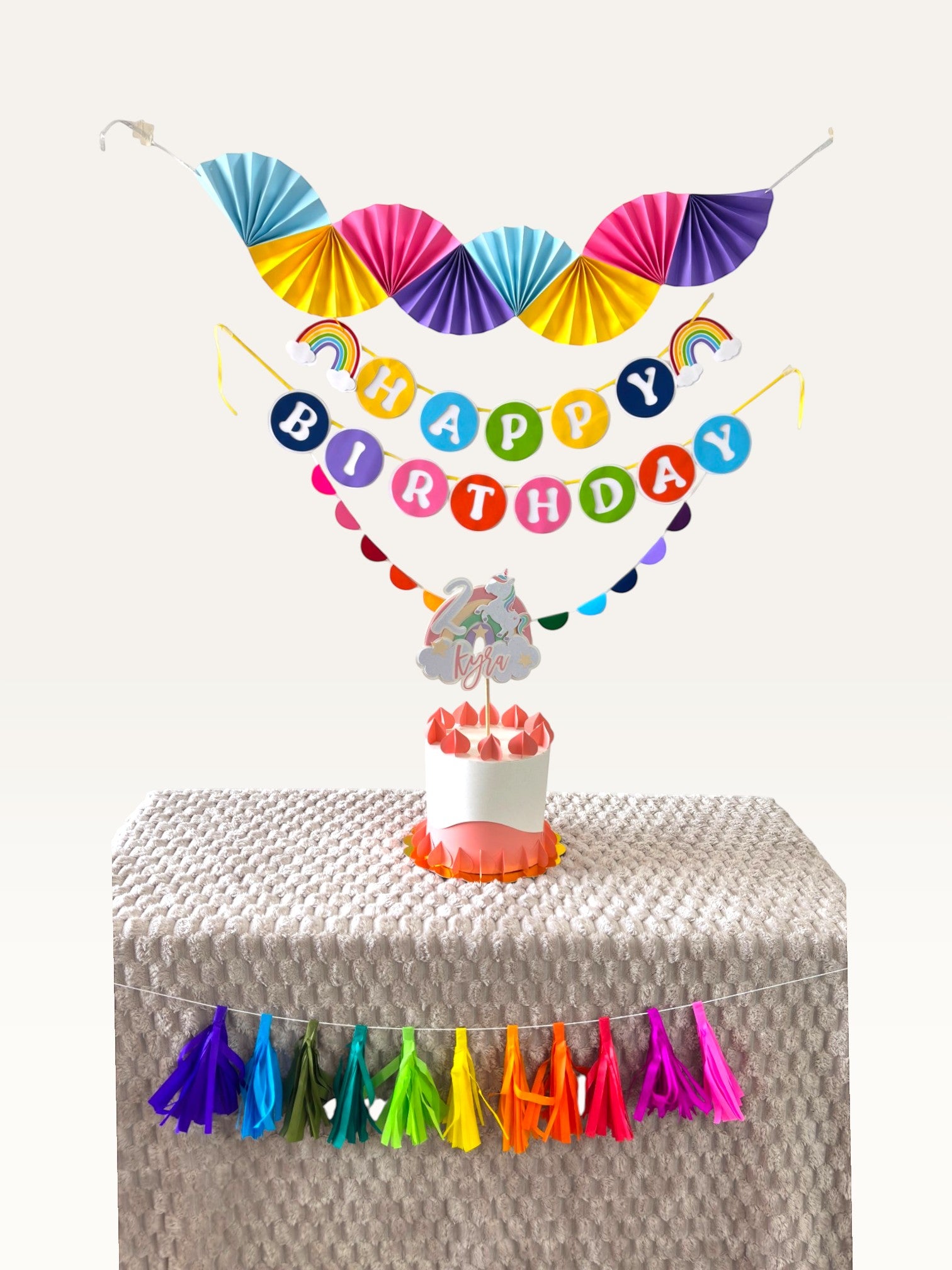 Paper Party Studio unicorn rainbow birthday party decoration set with personalised cake topper on a cake table
