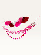 Paper Party Studio Valentine's decoration set with pink and red paper fan, I Love You banner, and scallop garland.