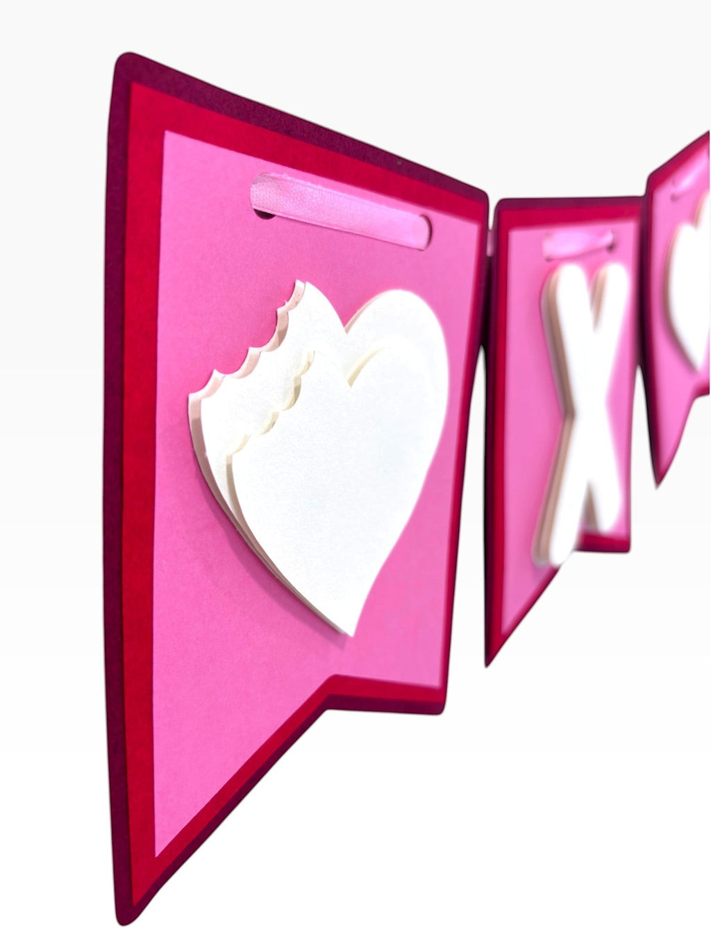 Paper Party Studio XOXO Valentine's banner with layered white hearts and letters on pink and red flags, tied with satin ribbon.