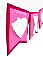 Paper Party Studio XOXO Valentine's banner with layered white hearts and letters on pink and red flags, tied with satin ribbon.