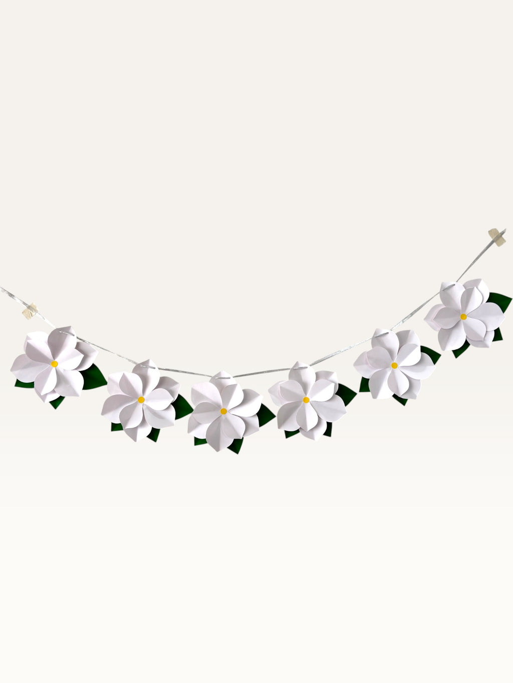 Paper Party Studio white 3D paper flower garland with yellow centers and green leaves on a silver hanging cord.