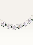 Paper Party Studio white 3D paper flower garland with yellow centers and green leaves on a silver hanging cord.