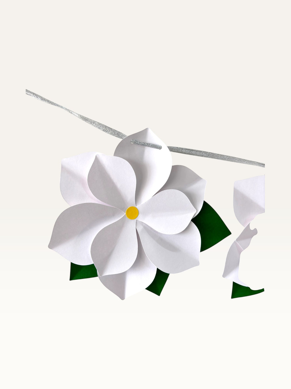Paper Party Studio white paper flower garland with layered blossoms, yellow centers, and green leaves on a silver cord.