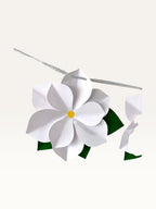 Paper Party Studio white paper flower garland with layered blossoms, yellow centers, and green leaves on a silver cord.