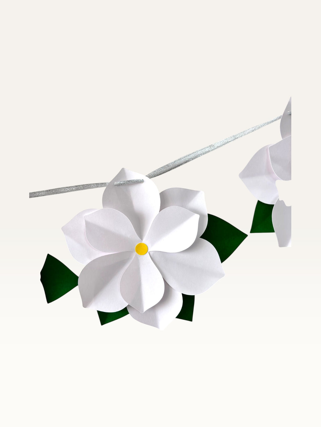 Paper Party Studio white 3D paper flower garland with yellow centers and green leaves on a silver hanging cord