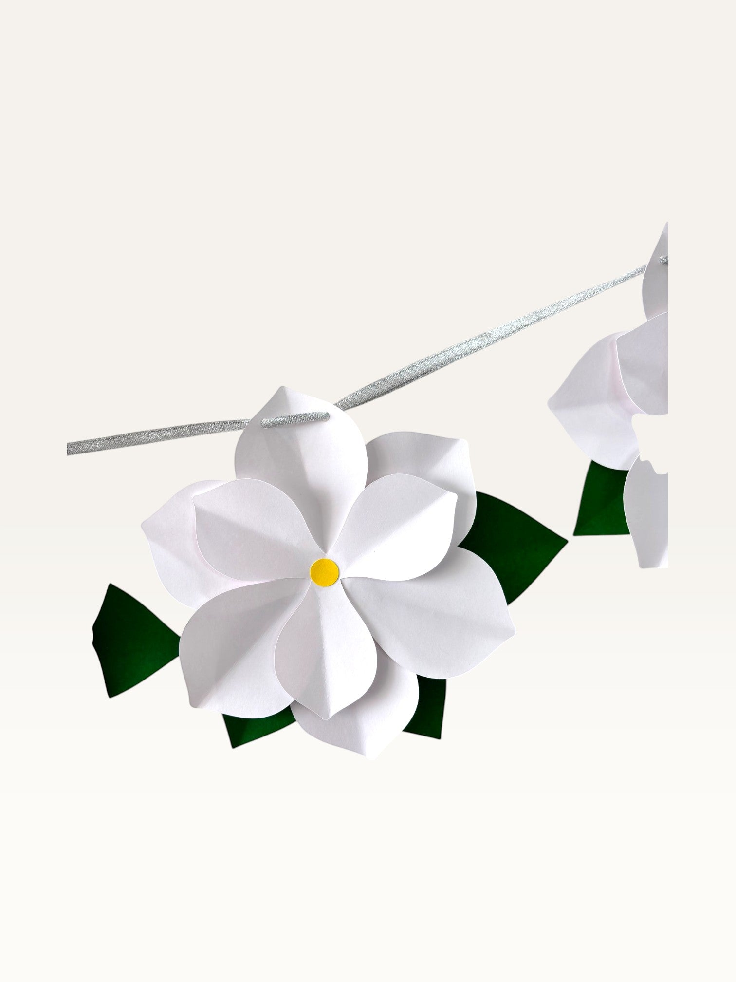 Paper Party Studio white 3D paper flower garland with yellow centers and green leaves on a silver hanging cord