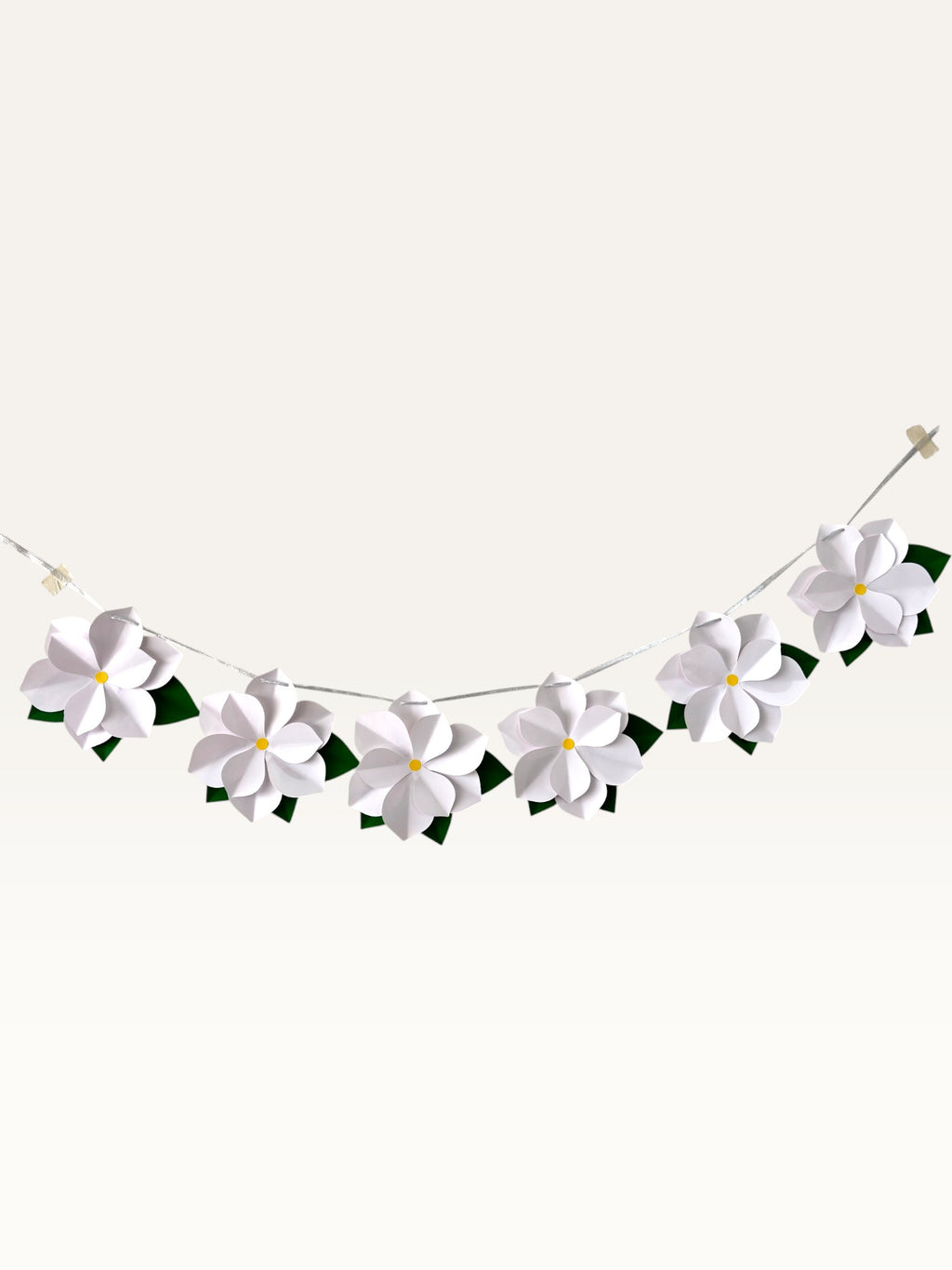 Paper Party Studio white paper flower garland with layered blossoms, yellow centers, and green leaves on a silver cord.