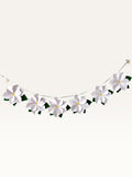 Paper Party Studio white paper flower garland with layered blossoms, yellow centers, and green leaves on a silver cord.