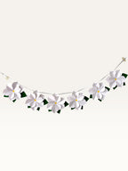 Paper Party Studio white paper flower garland with layered blossoms, yellow centers, and green leaves on a silver cord.