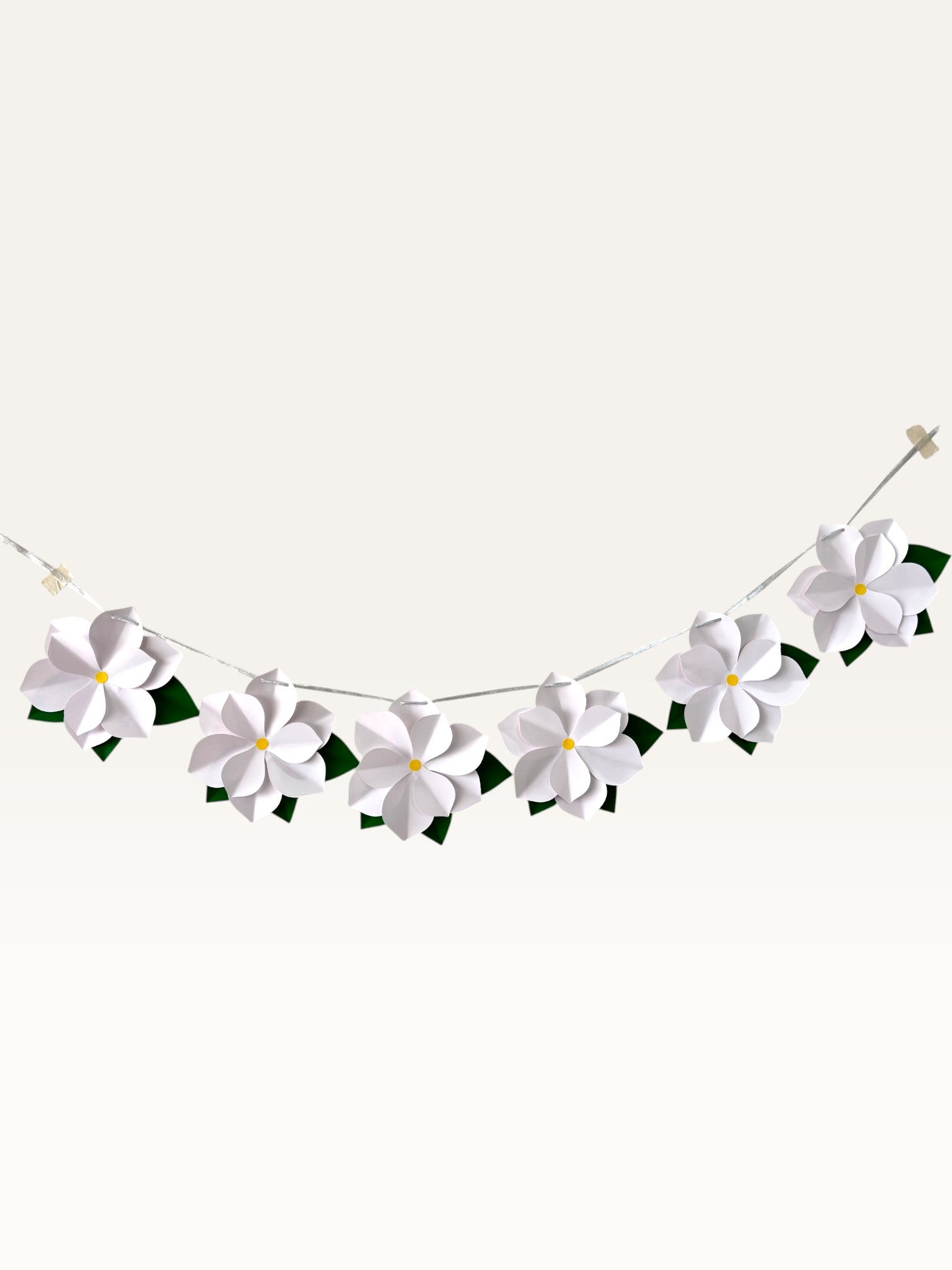 Paper Party Studio white paper flower garland with layered blossoms, yellow centers, and green leaves on a silver cord.