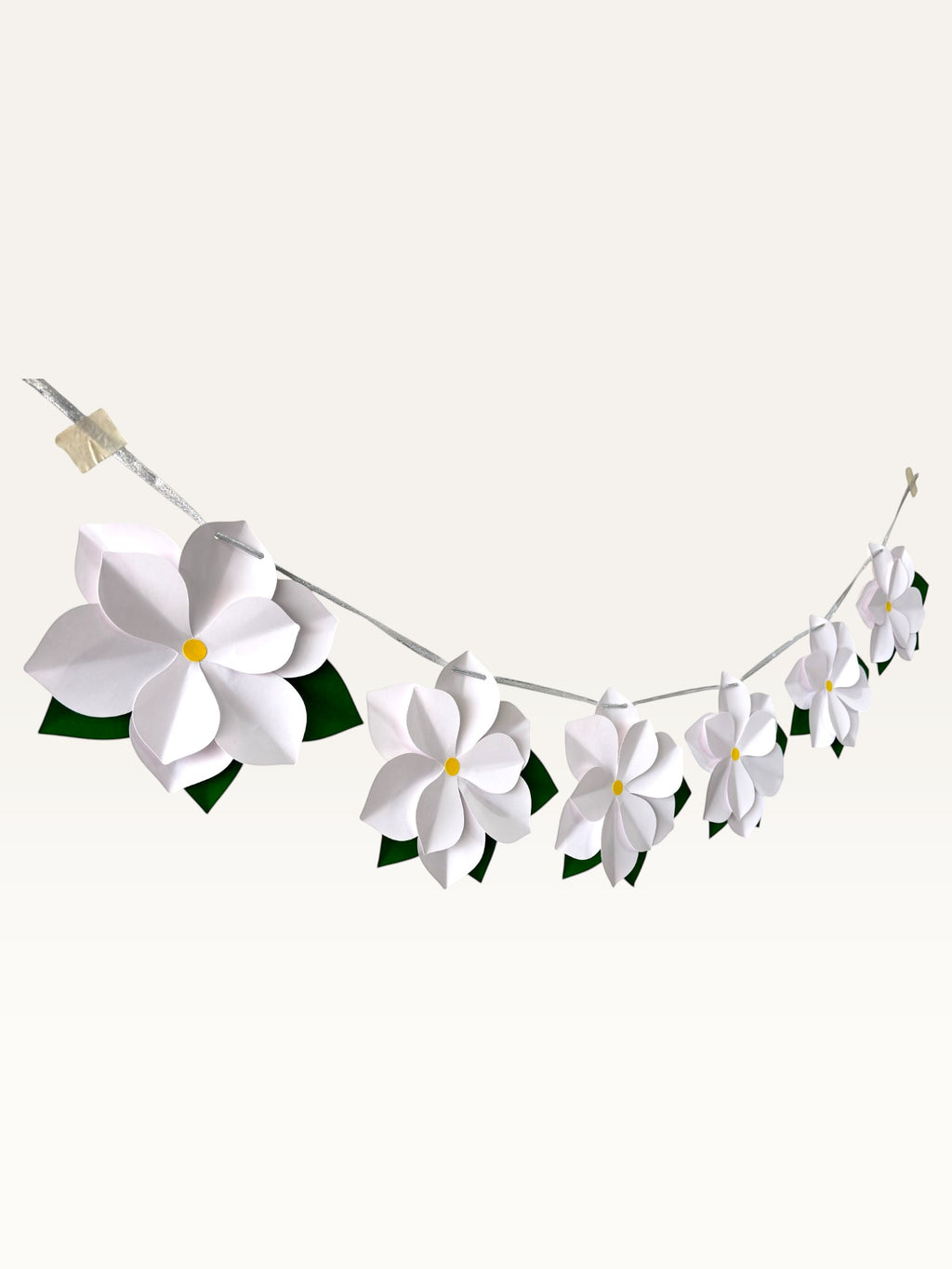 Paper Party Studio white paper flower garland with layered blossoms, yellow centers, and green leaves on a silver cord.