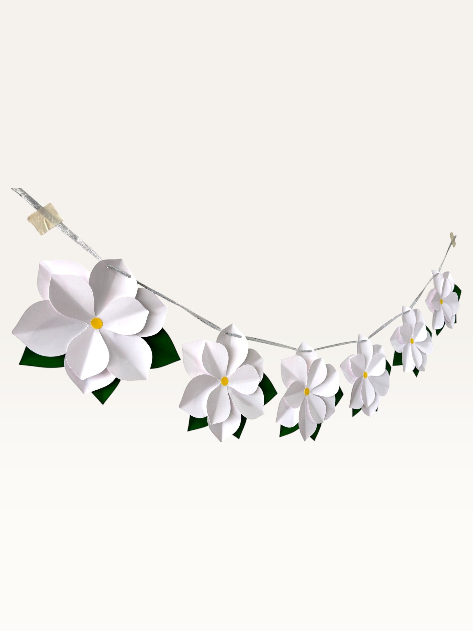 Paper Party Studio white paper flower garland with layered blossoms, yellow centers, and green leaves on a silver cord.