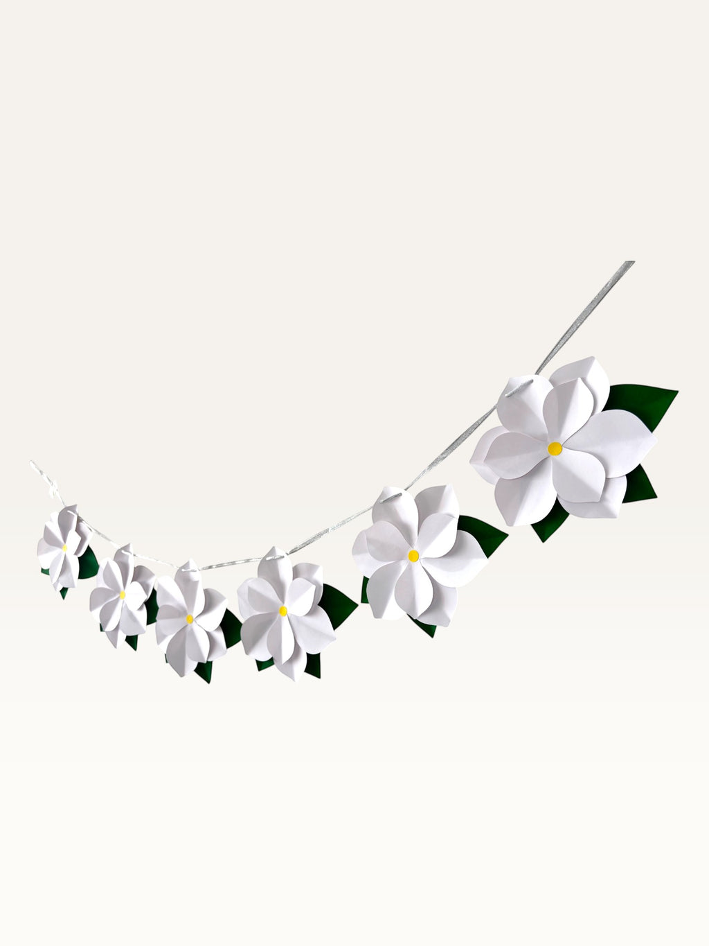 Paper Party Studio white 3D paper flower garland with yellow centers and green leaves on a silver hanging cord